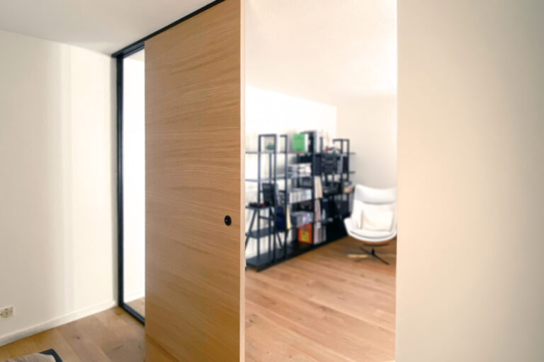 Blick vom Schlafzimmer in den offenen Wohnbereich – der Raum bleibt durch das Glasfeld lichtdurchflutet.