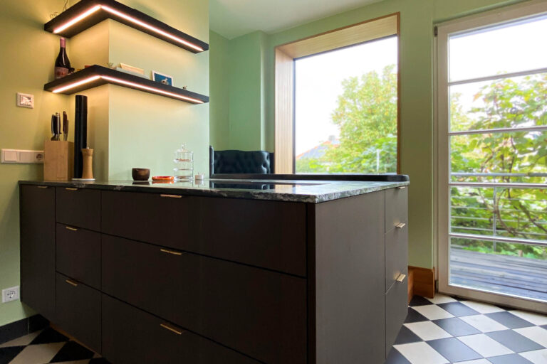 Küche mit gepolstertem Sitzfenster am schwarzen Eichentresen der Stein-Kochinsel mit Massivholzregalen und LED