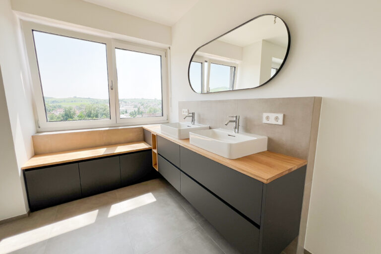 Waschtisch mit Sitzbank am Panoramafenster – maßgefertigtes Badezimmer mit viel Stauraum und Eichenauflage.
