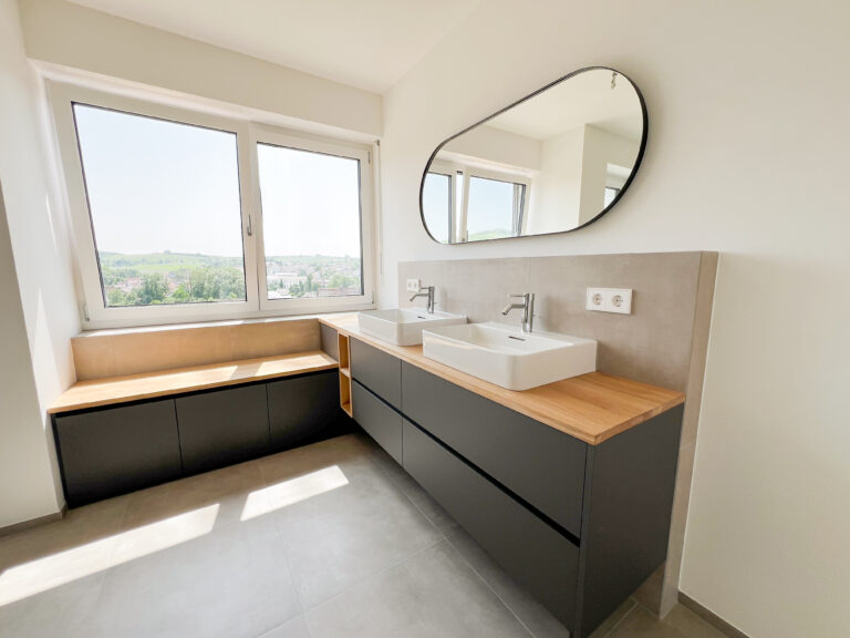 Waschtisch mit Sitzbank am Panoramafenster – maßgefertigtes Badezimmer mit viel Stauraum und Eichenauflage.