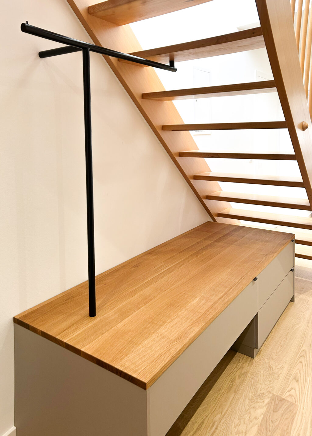 Garderobe unter Treppe mit Sitzbank und Kleiderstange – maßgefertigter Stauraum im Eingangsbereich mit Eiche und Stahl.